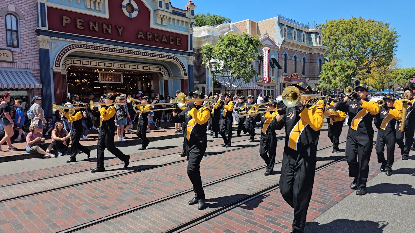 Brass players marching down a crowded parade route in the sunshine