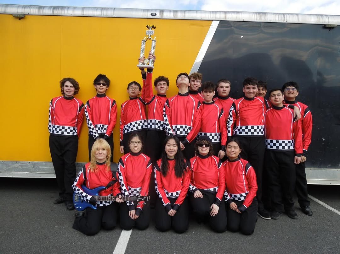 Band members in red and checkered racing jackets holding up a trophy