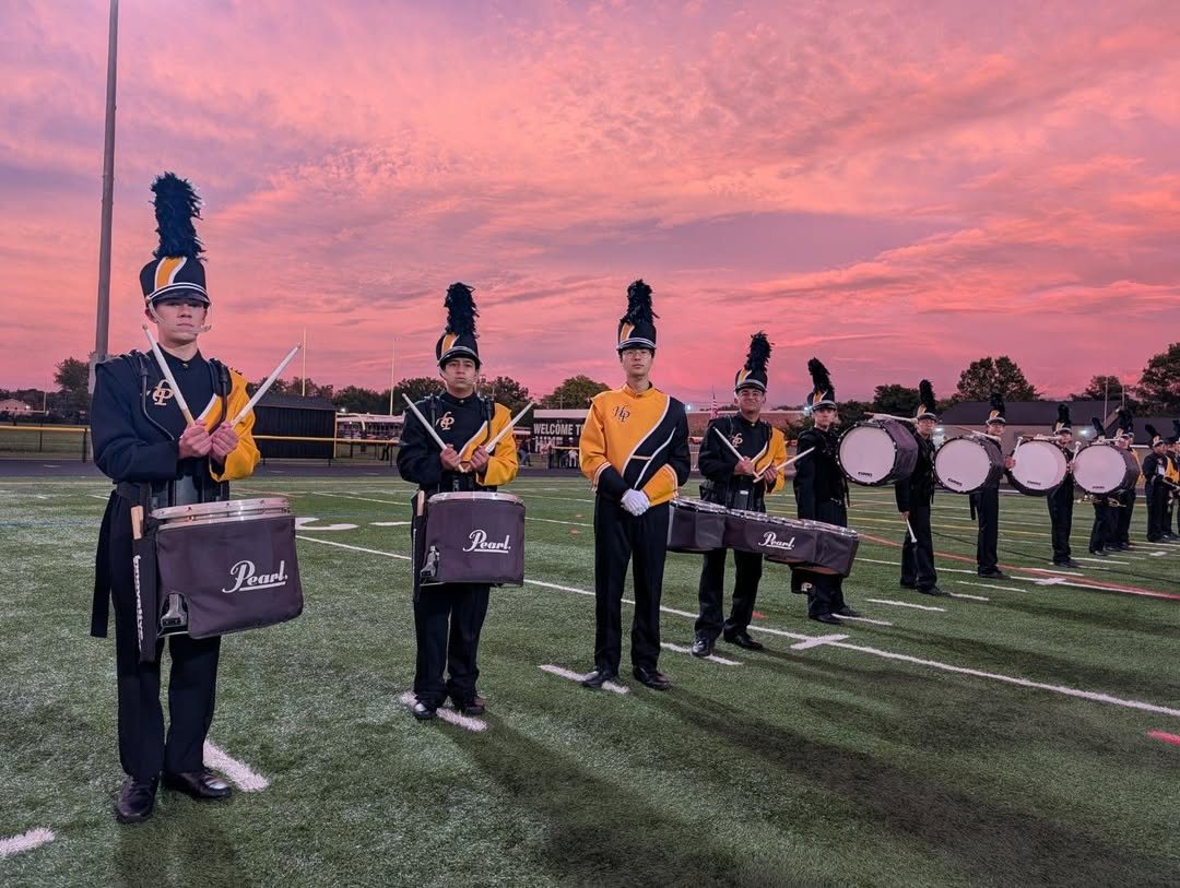 Drumline in uniform on the field under a pink sunset