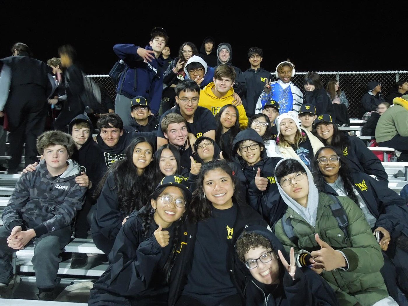 Band members in black jackets smiling together in the stands at night