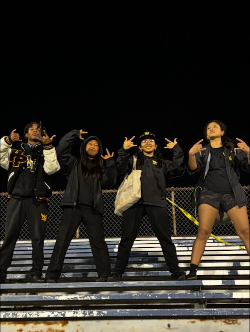 Four band members striking poses on the bleachers at night