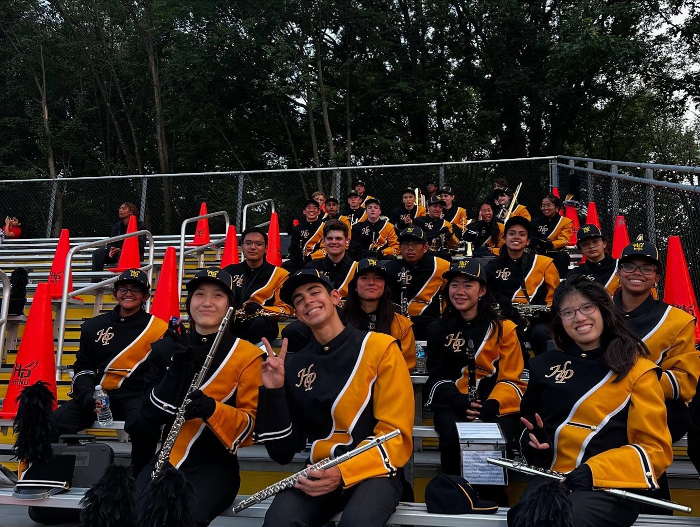Band members in uniform with flutes and clarinets sitting in the stands