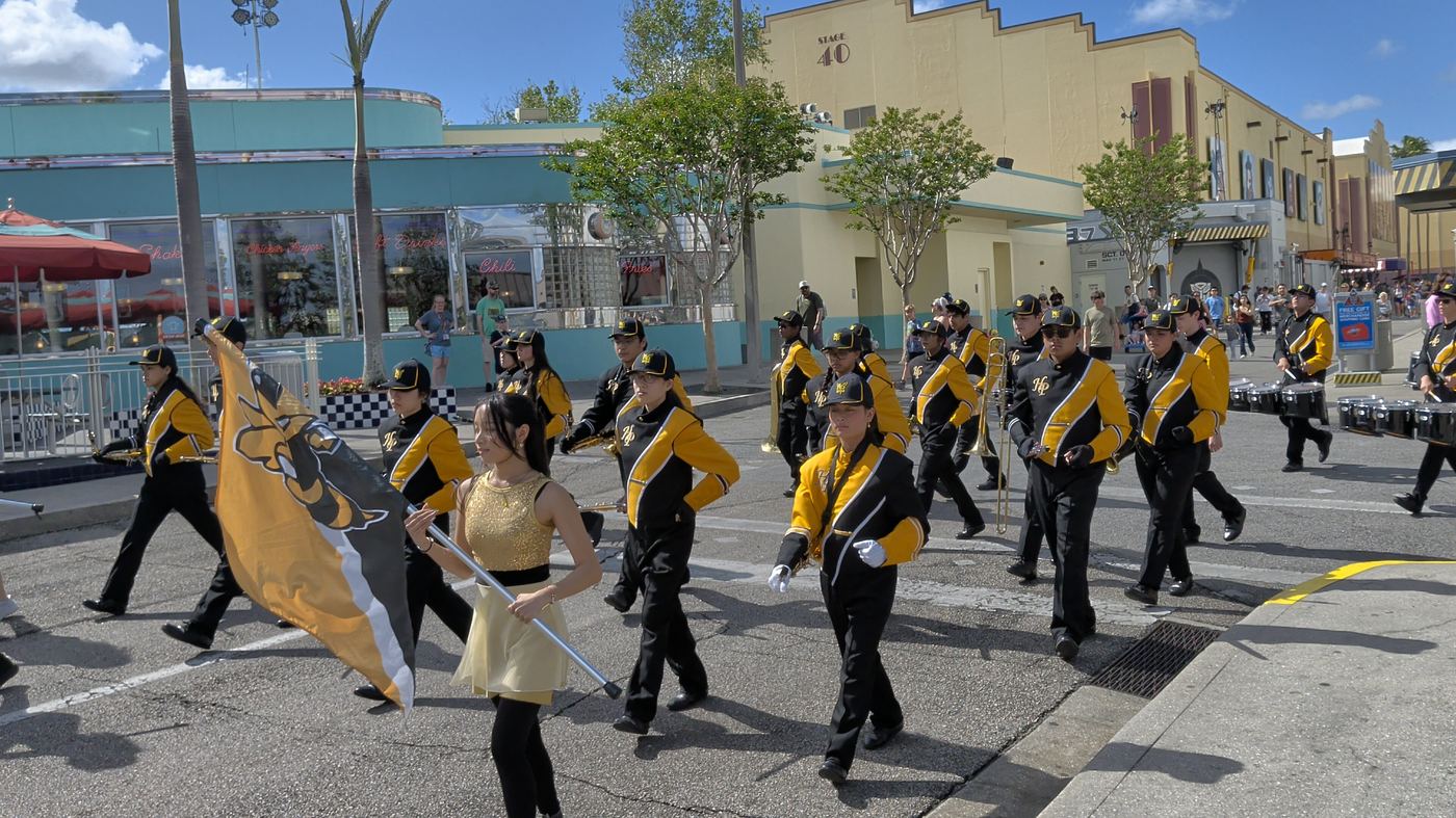 Color guard and band marching in a parade behind the hornet flag